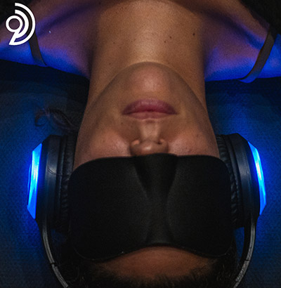 A woman lying down wearing an eye mask and 9D headphones
