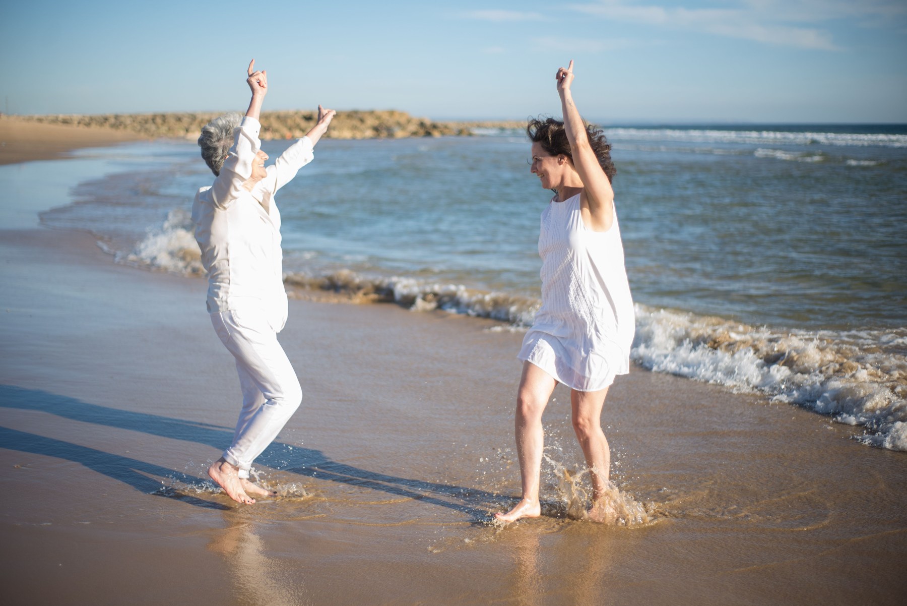 Two women laughing and dancing in the shallows at the beach